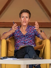 Prof. Dr. Christine Henschel sitzt in einem gelben Sessel. Sie hat kurze Haare und trägt eine geblümte Bluse. Sie gestikuliert mit den Händen.